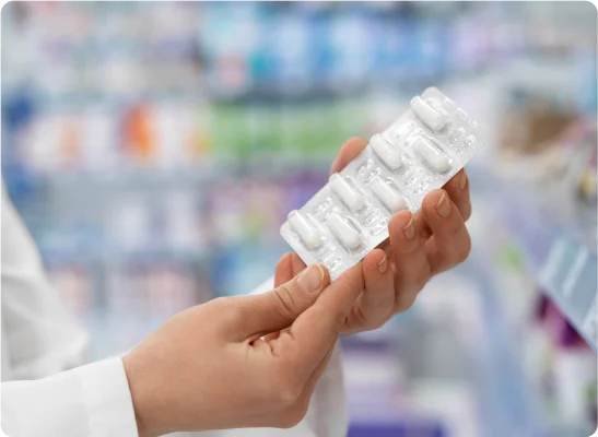 Person holding a pack of white capsules in a pharmacy.